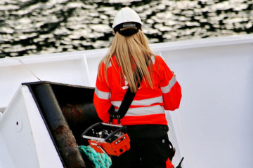 A woman working on deck of a coastal transport vessel in polar region of Norway; same job as for male colleagues on a big ship with heavy weather and equipment. Equal job = equal pay.