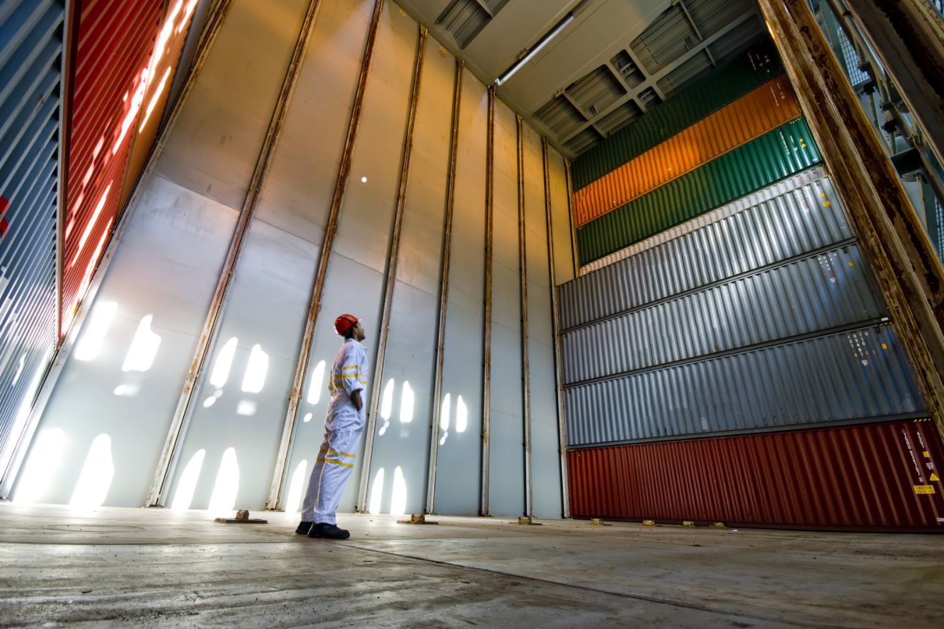 worker looking up at imposing stack of cargo containers